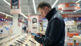 Giovane cliente maschio che sceglie un nuovo telefono cellulare in un negozio, controllante come funziona video d archivio Giovane cliente maschio che sceglie un nuovo telefono cellulare in un negozio, controllante come funziona video d archivio