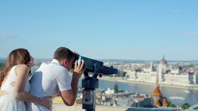Giovane con la donna al punto di osservazione facendo uso di binoculare a gettoni per vedere la bellezza della città video d archivio Giovane con la donna al punto di osservazione facendo uso di binoculare a gettoni per vedere la bellezza della città video d archivio