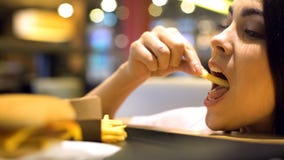 Giovane donna castana che mangia le patate fritte francesi, piacere degli alimenti industriali, pasto immagini stock libere da diritti Giovane donna castana che mangia le patate fritte francesi, piacere degli alimenti industriali, pasto immagini stock libere da diritti