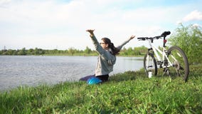 Giovane donna che guida una bici attraverso il parco sui precedenti di un lago o di un fiume video d archivio Giovane donna che guida una bici attraverso il parco sui precedenti di un lago o di un fiume video d archivio