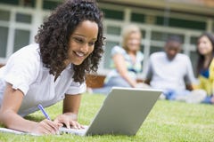 Giovane donna che per mezzo del computer portatile sul prato inglese della città universitaria immagini stock libere da diritti Giovane donna che per mezzo del computer portatile sul prato inglese della città universitaria immagini stock libere da diritti