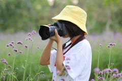 Giovane donna che tiene la macchina fotografica di DSLR in sue mani e che sta sui fiori fondo, concetto di vacanze di stile di vi immagini stock Giovane donna che tiene la macchina fotografica di DSLR in sue mani e che sta sui fiori fondo, concetto di vacanze di stile di vi immagini stock