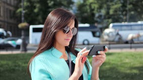 Giovane donna entusiasta di viaggio in occhiali da sole facendo uso dello smartphone al fondo soleggiato di paesaggio urbano archivi video Giovane donna entusiasta di viaggio in occhiali da sole facendo uso dello smartphone al fondo soleggiato di paesaggio urbano archivi video