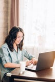Giovane donna felice che per mezzo del computer portatile a casa immagine stock libera da diritti Giovane donna felice che per mezzo del computer portatile a casa immagine stock libera da diritti