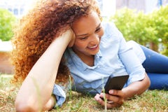 Giovane donna felice che si trova nell'erba al parco e che esamina telefono cellulare fotografia stock libera da diritti Giovane donna felice che si trova nell'erba al parco e che esamina telefono cellulare fotografia stock libera da diritti