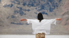 Giovane donna locale libera felice di vista posteriore che cammina alla montagna epica che alza armi nel lago del deserto del sal stock footage Giovane donna locale libera felice di vista posteriore che cammina alla montagna epica che alza armi nel lago del deserto del sal stock footage