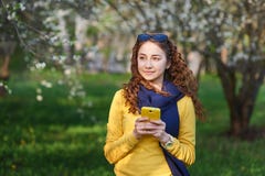 Giovane donna nel giardino sbocciante della molla con lo smartphone immagini stock Giovane donna nel giardino sbocciante della molla con lo smartphone immagini stock