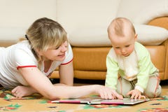 Giovane lettura della mamma il suo piccolo libro del figlio su un pavimento fotografia stock libera da diritti Giovane lettura della mamma il suo piccolo libro del figlio su un pavimento fotografia stock libera da diritti