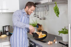 Giovane nella cucina che cucina le uova fritte fotografia stock Giovane nella cucina che cucina le uova fritte fotografia stock