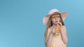 Giovane ragazza dell'adolescente in vetri gialli e cocktail bevente del cappello sullo schermo blu video d archivio Giovane ragazza dell'adolescente in vetri gialli e cocktail bevente del cappello sullo schermo blu video d archivio