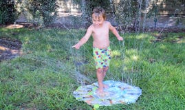 Giovane ragazzo che gioca in uno spruzzatore del prato inglese Immagini Stock Giovane ragazzo che gioca in uno spruzzatore del prato inglese Immagini Stock