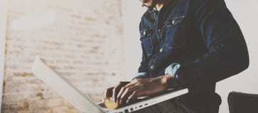 Giovane uomo africano barbuto che per mezzo del computer portatile mentre sedendosi al suo posto coworking moderno Concetto della Immagini Stock Giovane uomo africano barbuto che per mezzo del computer portatile mentre sedendosi al suo posto coworking moderno Concetto della Immagini Stock