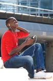 Giovane uomo africano che gode della musica d'ascolto sul telefono cellulare fotografia stock Giovane uomo africano che gode della musica d'ascolto sul telefono cellulare fotografia stock