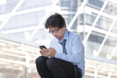 Giovane uomo asiatico disoccupato che cerca lavoro in Smart Phone mobile al fondo della città Concetto di disoccupazione immagini stock libere da diritti Giovane uomo asiatico disoccupato che cerca lavoro in Smart Phone mobile al fondo della città Concetto di disoccupazione immagini stock libere da diritti