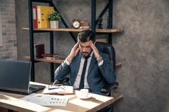 Giovane uomo d'affari bello alla moda che lavora al suo scrittorio nell'ufficio ha un'emicrania terribile immagini stock libere da diritti Giovane uomo d'affari bello alla moda che lavora al suo scrittorio nell'ufficio ha un'emicrania terribile immagini stock libere da diritti