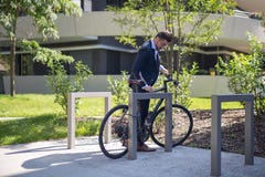 Giovane uomo d'affari bello che parcheggia la sua bicicletta sul lavoro immagine stock Giovane uomo d'affari bello che parcheggia la sua bicicletta sul lavoro immagine stock