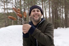 Giovane uomo sorridente che tiene una salsiccia su uno sputo nel legno fotografia stock Giovane uomo sorridente che tiene una salsiccia su uno sputo nel legno fotografia stock