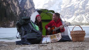 Giovane viaggio delle coppie Sedendosi nella tenda e cantare dalla chitarra su un fondo delle montagne stock footage Giovane viaggio delle coppie Sedendosi nella tenda e cantare dalla chitarra su un fondo delle montagne stock footage