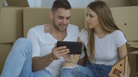 Giovani coppie che si siedono sul pavimento facendo uso del computer della compressa dopo il reloction nella loro nuova casa archivi video Giovani coppie che si siedono sul pavimento facendo uso del computer della compressa dopo il reloction nella loro nuova casa archivi video