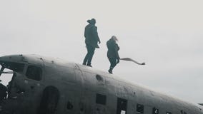 Giovani coppie di viaggio che camminano sulla cima dell'aereo caduto DC-3 in Islanda nel giorno nuvoloso ventoso video d archivio Giovani coppie di viaggio che camminano sulla cima dell'aereo caduto DC-3 in Islanda nel giorno nuvoloso ventoso video d archivio