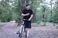 Giovani spume caucasiche dell'uomo tramite il telefono cellulare che va in bicicletta nel parco fotografia stock libera da diritti Giovani spume caucasiche dell'uomo tramite il telefono cellulare che va in bicicletta nel parco fotografia stock libera da diritti