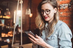 Girl blogger in trendy glasses sits in cafe and uses smartphone,checks e-mail,communicates with followers,reads news. stock photo Girl blogger in trendy glasses sits in cafe and uses smartphone,checks e-mail,communicates with followers,reads news. stock photo