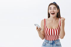 Girl cannot believe miracle happened being surprised and happy clenching fist in success and victory holding smartphone stock photo Girl cannot believe miracle happened being surprised and happy clenching fist in success and victory holding smartphone stock photo