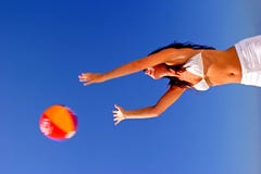 Girl catching beach ball on sunny beach in Spain with blue sky