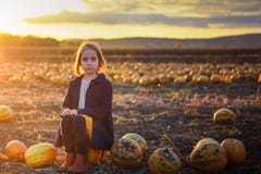 Girl in dark blue coat sits on a pumpkin on the field on sunset. Halloween royalty free stock photo Girl in dark blue coat sits on a pumpkin on the field on sunset. Halloween royalty free stock photo