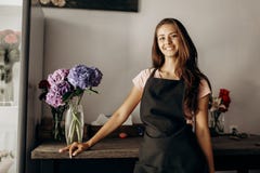 Girl florist in a black apron stands near the table with a vase with blue and lilac hydrangea stock images Girl florist in a black apron stands near the table with a vase with blue and lilac hydrangea stock images