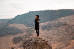 The girl holds her hat, turning her back to the valley with the mountains. stay on rock royalty free stock image The girl holds her hat, turning her back to the valley with the mountains. stay on rock royalty free stock image