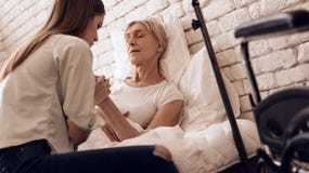 Girl is nursing elderly woman at home. They are holding hands. Wheelchair is standing near. stock image Girl is nursing elderly woman at home. They are holding hands. Wheelchair is standing near. stock image