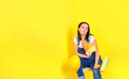Girl painter with a roller in his helmet sits near a painted wall with a palette of color choices royalty free stock image Girl painter with a roller in his helmet sits near a painted wall with a palette of color choices royalty free stock image