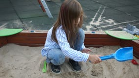 Girl preschool girl with long hair plays in the sandbox with a shovel and apiary. Happy childhood. Weekdays at the