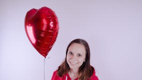 A girl in a red sweatshirt in her hand a red balloon in the form of a heart. Student posing on white background stock photography A girl in a red sweatshirt in her hand a red balloon in the form of a heart. Student posing on white background stock photography