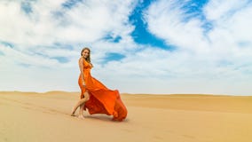 Girl Smiles, Walks On Desert In Dress Fluttering In Wind. Happy Woman Is Walking, Staing On Sand Or Dune, Touches, Shows Stock Image Girl Smiles, Walks On Desert In Dress Fluttering In Wind. Happy Woman Is Walking, Staing On Sand Or Dune, Touches, Shows Stock Image