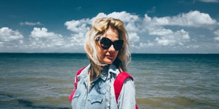 Girl traveler with a backpack stands on the background of the sea and enjoys the beautiful scenery. Concept of travel, adventure, stock photo Girl traveler with a backpack stands on the background of the sea and enjoys the beautiful scenery. Concept of travel, adventure, stock photo