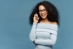 Glad African American-het wijfje geniet telefoon van gesprek, houdt één overhandigt taille, gebruik de moderne technologieën, bri royalty-vrije stock afbeelding Glad African American-het wijfje geniet telefoon van gesprek, houdt één overhandigt taille, gebruik de moderne technologieën, bri royalty-vrije stock afbeelding