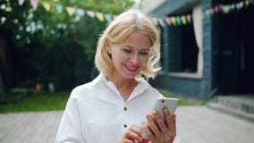 Glad kvinna som använder smartphonen som ser skärmen som utomhus ler anseende arkivfilmer Glad kvinna som använder smartphonen som ser skärmen som utomhus ler anseende arkivfilmer