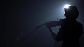 Glare from a lantern in a dark studio where a musician plays the violin. Black smoke background. Back view stock video footage Glare from a lantern in a dark studio where a musician plays the violin. Black smoke background. Back view stock video footage