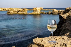 Glass of cold white dry white wine served on rocks in blue sea bay near Protaras touristic town on Cyprus
