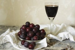 Glass of dessert wine and a plate of fresh plums on a light background in rustic style Royalty Free Stock Photography Glass of dessert wine and a plate of fresh plums on a light background in rustic style Royalty Free Stock Photography