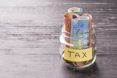 Glass jar on a black wooden table with coins and euro banknotes and the words TAX royalty free stock photo Glass jar on a black wooden table with coins and euro banknotes and the words TAX royalty free stock photo