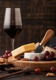 Glass of red wine with selection of various cheese on the board and grapes on wooden background. Blue Stilton, Red Leicester and. Glass of red wine with