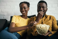 glimlachend jong Afrikaans Amerikaans paar die popcorn eten terwijl het zitten op bank royalty-vrije stock afbeelding glimlachend jong Afrikaans Amerikaans paar die popcorn eten terwijl het zitten op bank royalty-vrije stock afbeelding