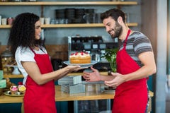 Glimlachende serveerster die een plaat van cake geven aan kelner Stock Afbeelding Glimlachende serveerster die een plaat van cake geven aan kelner Stock Afbeelding