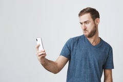 Playful caucasian man with dark hair, blue eyes and beard holding mobile phone, posing for selfie, making faces. Good stock image Playful caucasian man with dark hair, blue eyes and beard holding mobile phone, posing for selfie, making faces. Good stock image