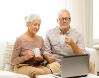 Glückliche ältere Paare mit Laptop und Schalen zu Hause Lizenzfreie Stockfotografie Glückliche ältere Paare mit Laptop und Schalen zu Hause Lizenzfreie Stockfotografie