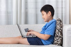 Glücklicher asiatischer chinesischer kleiner Junge, der Laptop mit Kreditkarte verwendet Lizenzfreie Stockfotos Glücklicher asiatischer chinesischer kleiner Junge, der Laptop mit Kreditkarte verwendet Lizenzfreie Stockfotos