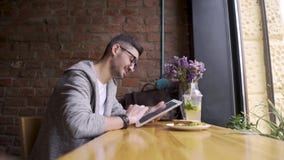 Glücklicher netter männlicher Student, der Tablet-Computer verwendet Kerl, der in einem Café mit einer Tablette in ihren Händen s stock video Glücklicher netter männlicher Student, der Tablet-Computer verwendet Kerl, der in einem Café mit einer Tablette in ihren Händen s stock video